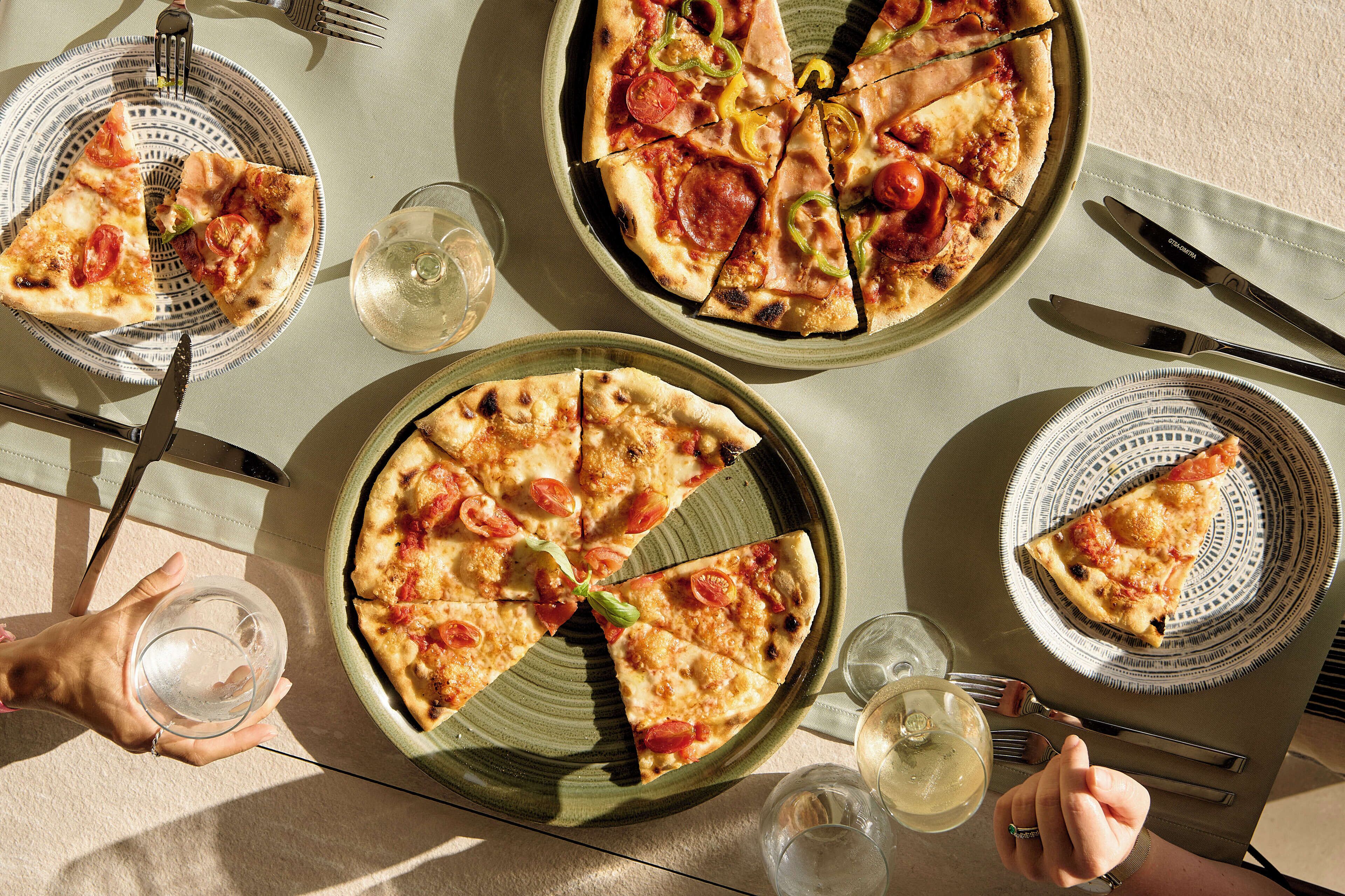 Een tafel met drie pizza's, bestek en glazen water.