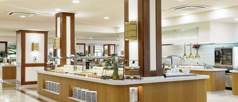 En moderne hotellobby med en central receptionsdisk, et buffetområde og et køkken i baggrunden.