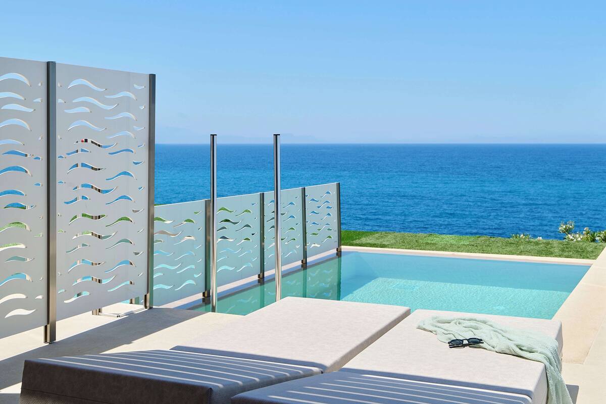Un espace aménagé au bord de la piscine, avec des chaises longues, une vue dégagée sur l’océan et une clôture décorative.