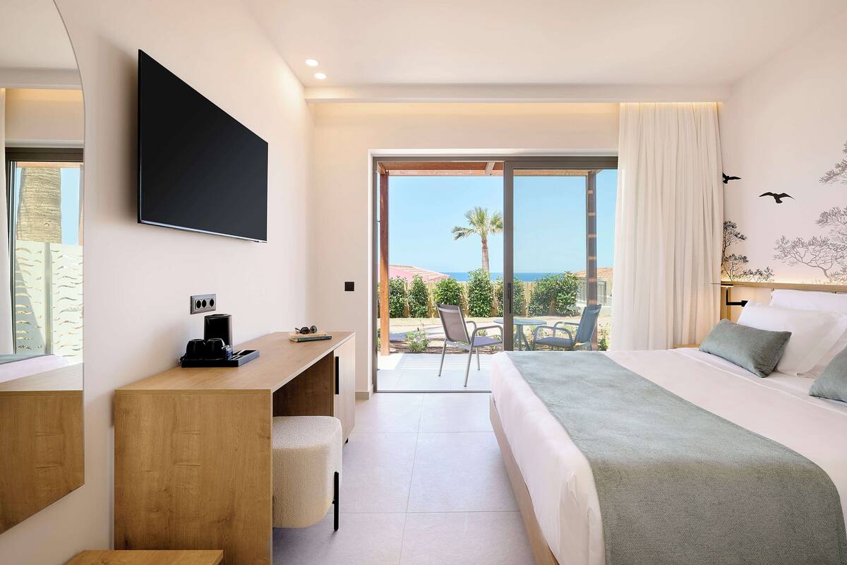 Une chambre d’hôtel moderne équipée d’un lit, d’un bureau, d’une chaise et d’une grande fenêtre donnant sur l’extérieur.