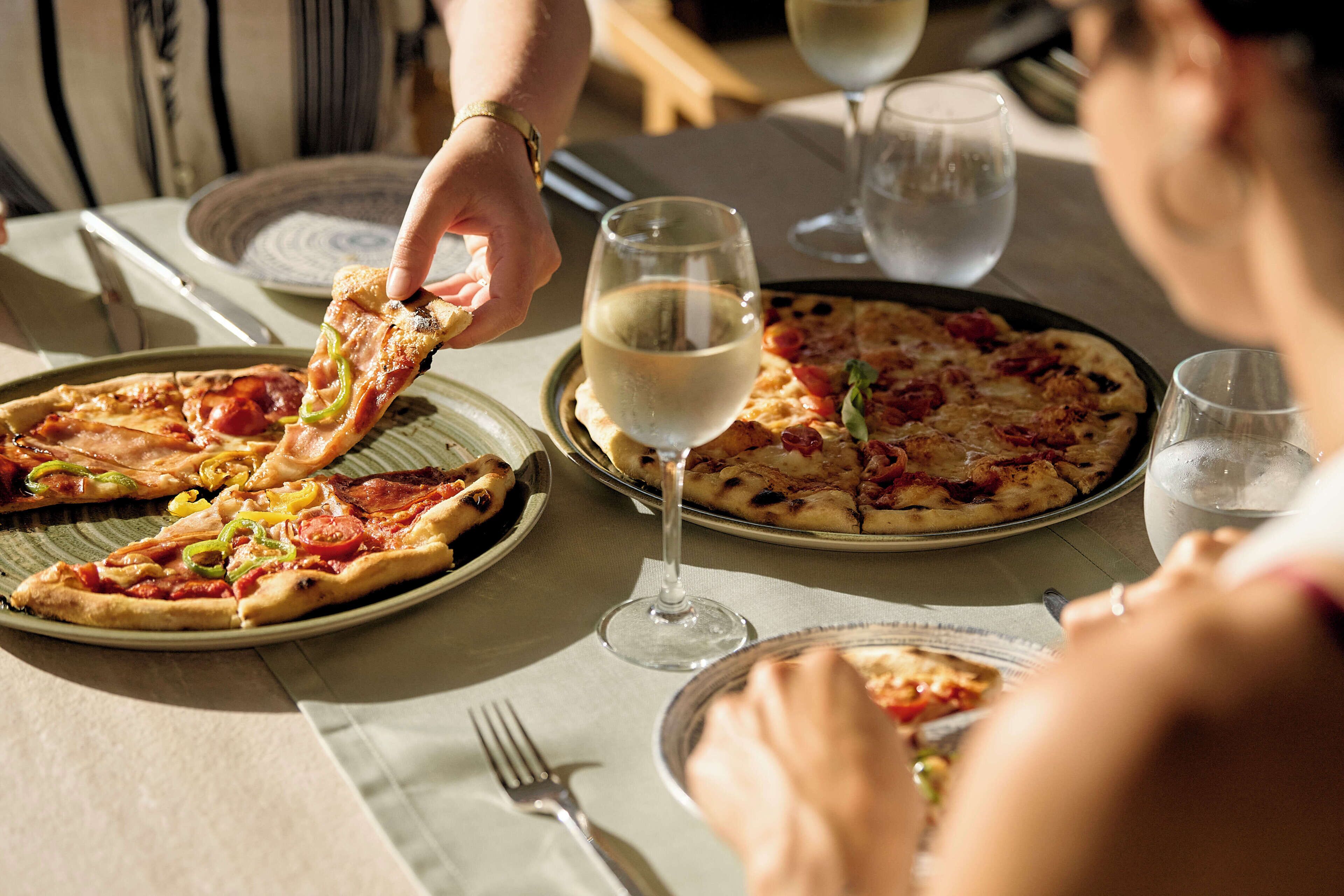 A dining table with pizza, wine glasses, and plates.