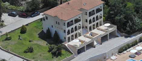 A multi-story building with a tiled roof, a swimming pool, and a parking area.