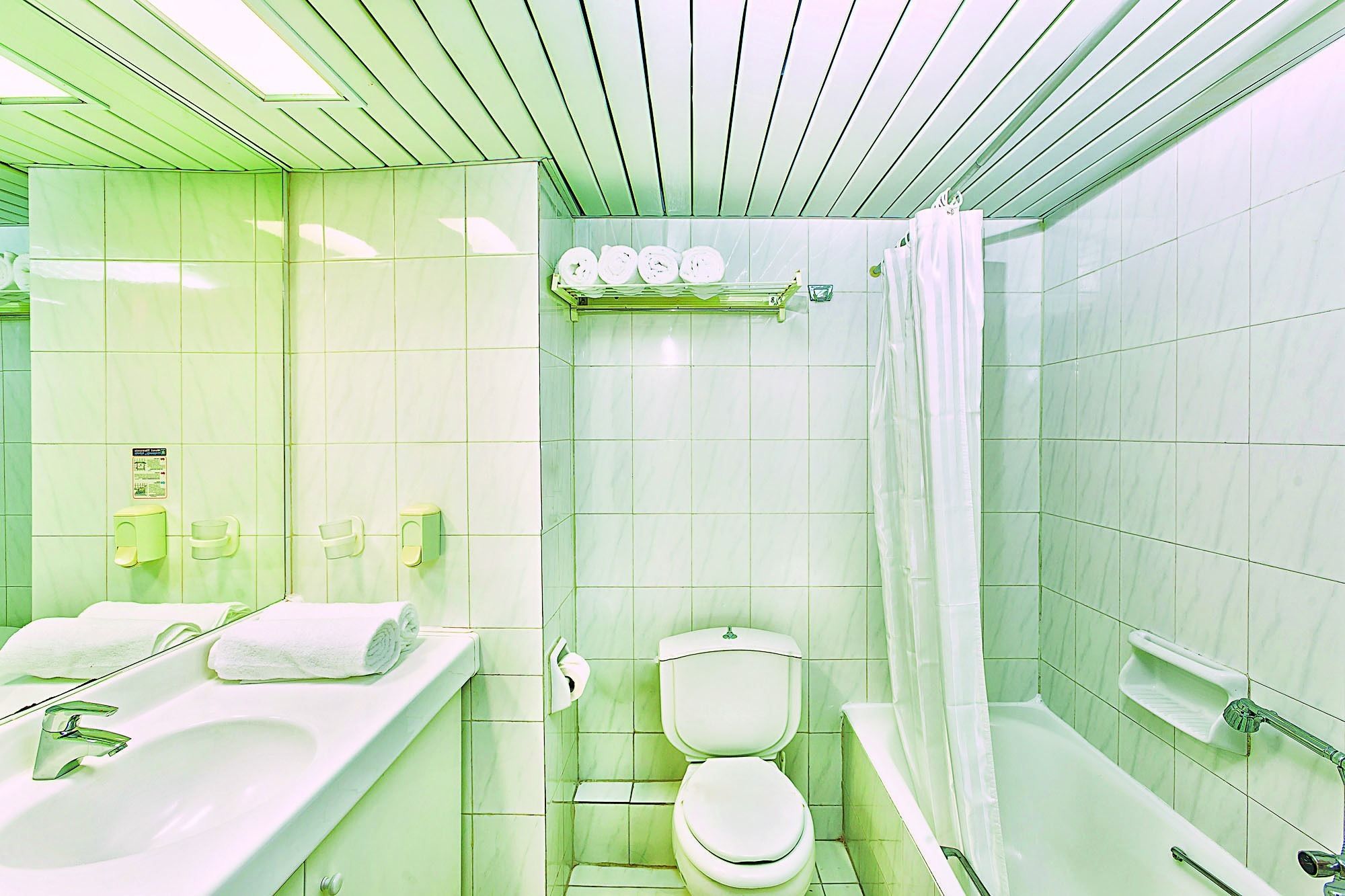 A bathroom with a sink, toilet, and shower area, all with green tiles.