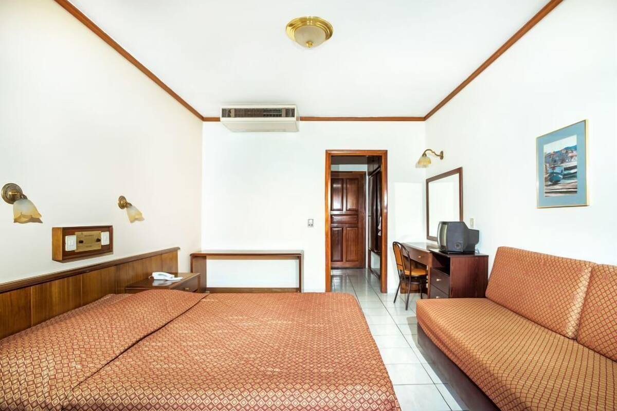 Ein Hotelzimmer mit einem Bett, einem Schlafsofa, einem Schreibtisch mit Stuhl, einem Fernseher und einer Klimaanlage.
