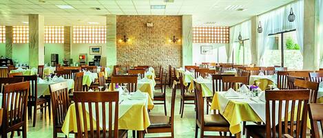 Un restaurante espacioso con varias mesas y sillas, un revestimiento de pared de piedra y amplios ventanales que dejan entrar la luz natural.
