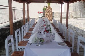 Ein langer Tisch, gedeckt für ein festliches Essen im Freien, mit weißen Stühlen und einer weißen Tischdecke.