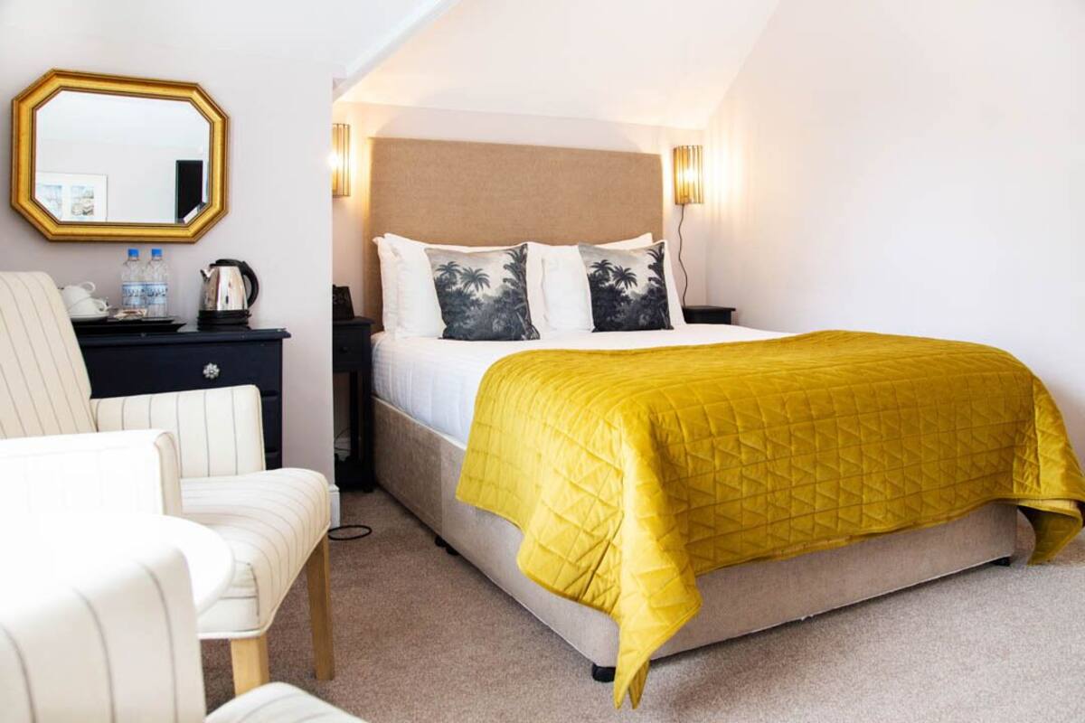 A bedroom with a bed, a nightstand, a chair, a mirror, and a wall-mounted light fixture.