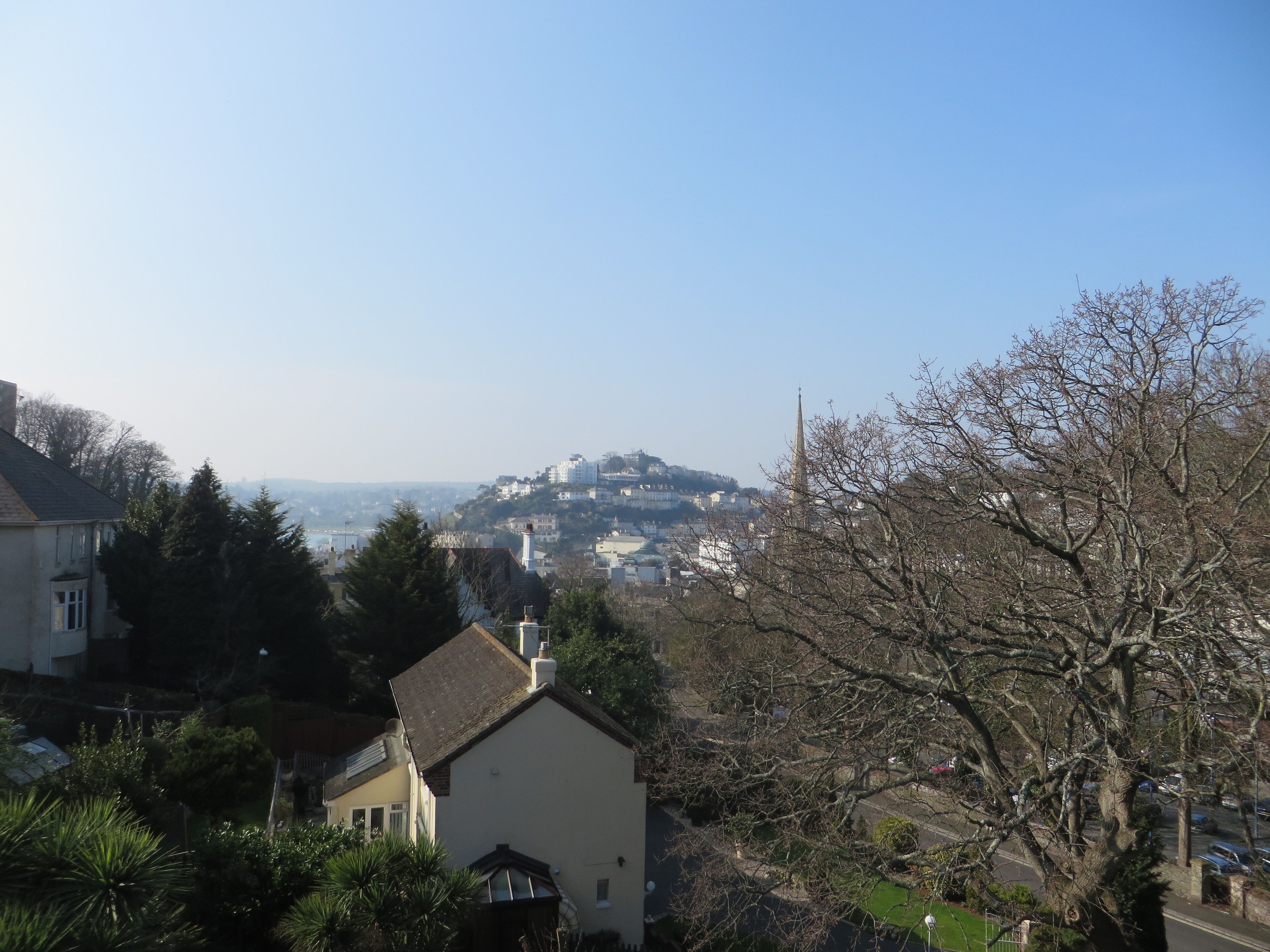 A residential area with houses, a church, and a hill with buildings in the background.