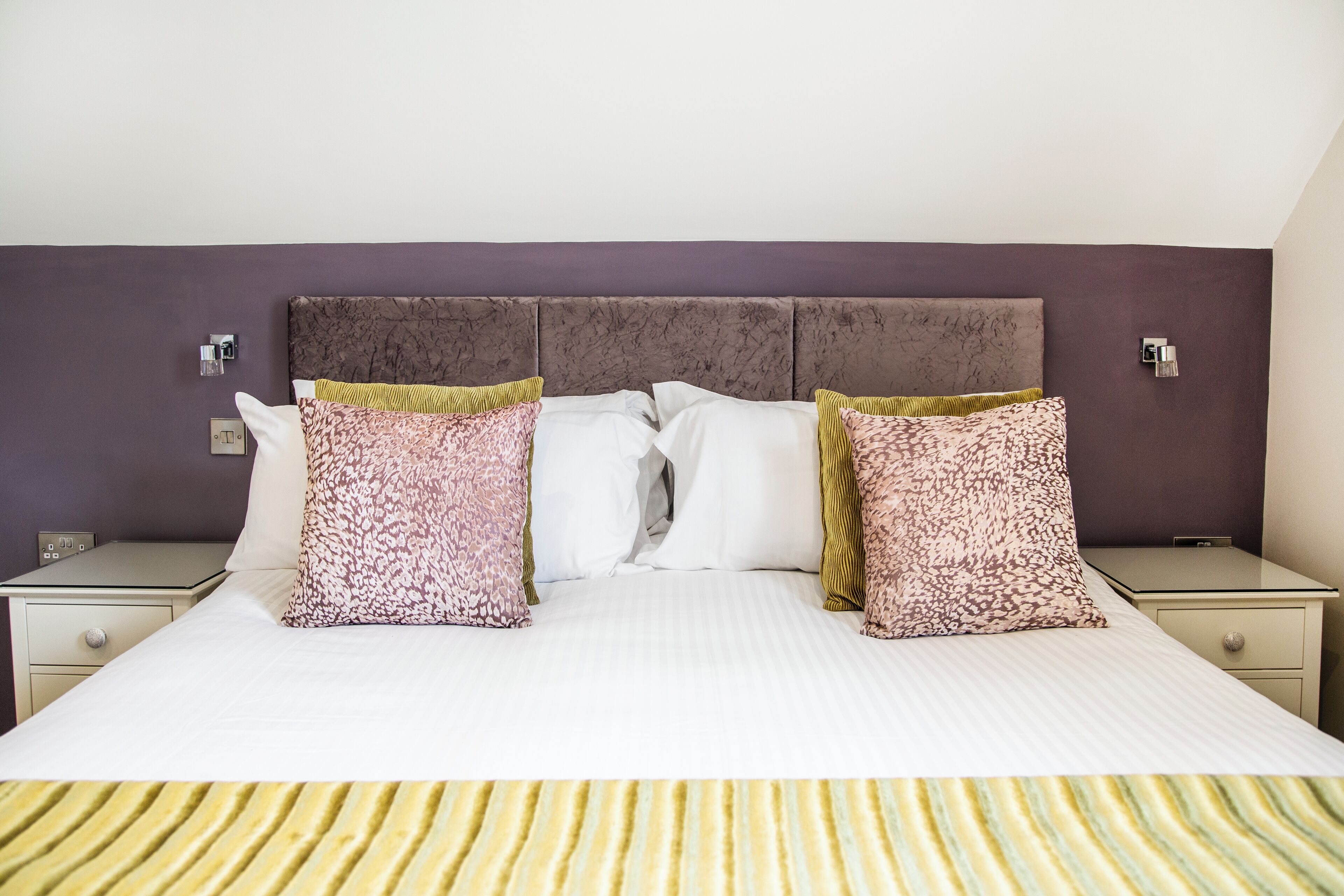 A neatly made bed with patterned pillows, a headboard, and bedside tables with lamps.