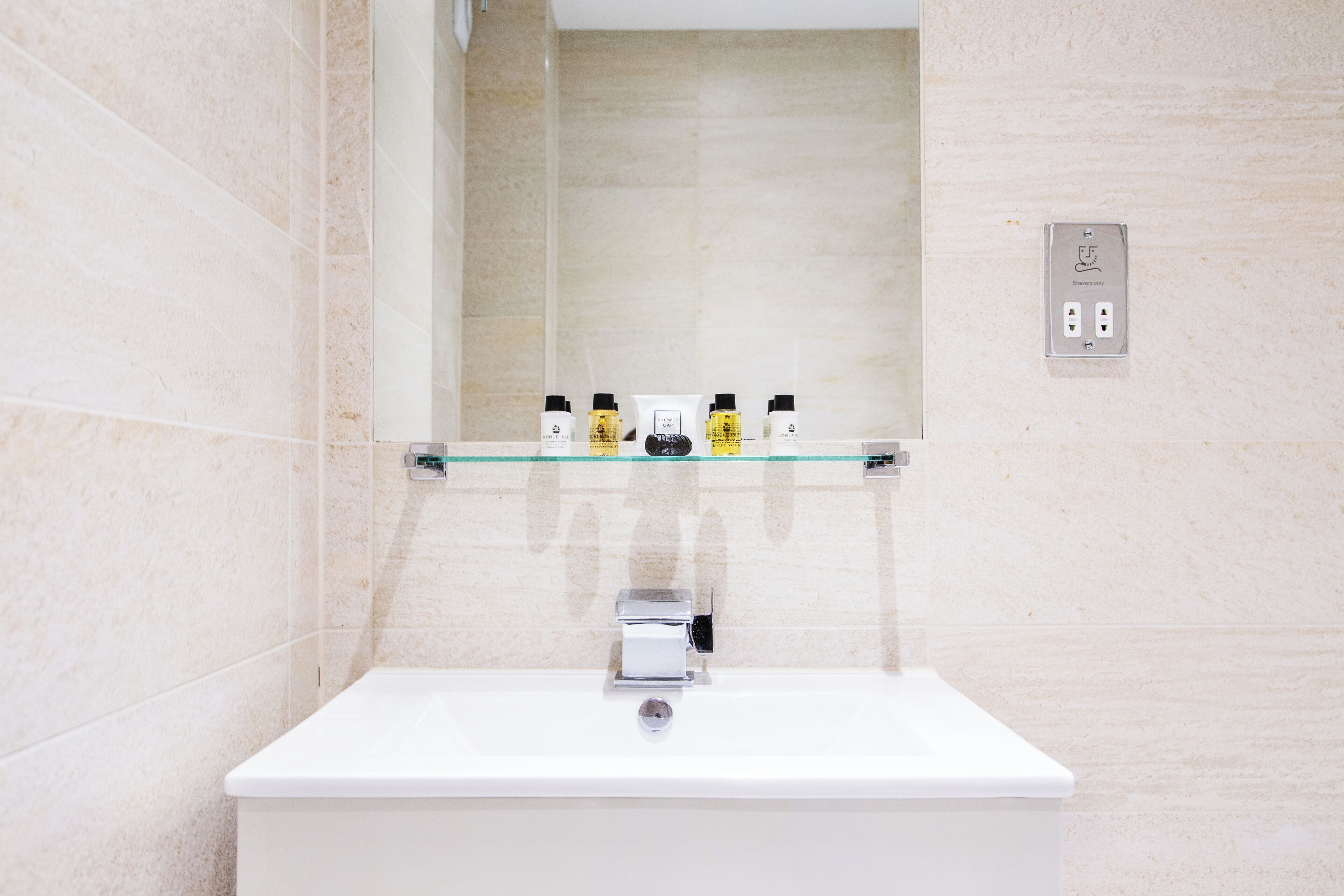 A bathroom with a white sink, a glass shelf with toiletries, and a shower control panel.
