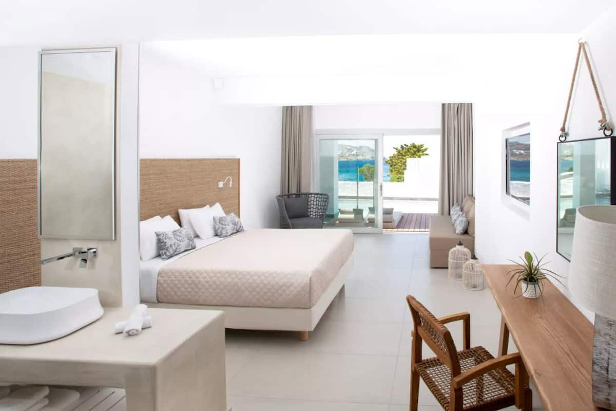 Un moderno cuarto de hotel con una cama grande, un escritorio, una silla, un baño con lavamanos y un balcón con vista al mar.