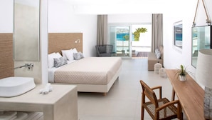 A modern hotel room with a large bed, a desk, a chair, a bathroom with a sink, and a balcony with a view of the sea.
