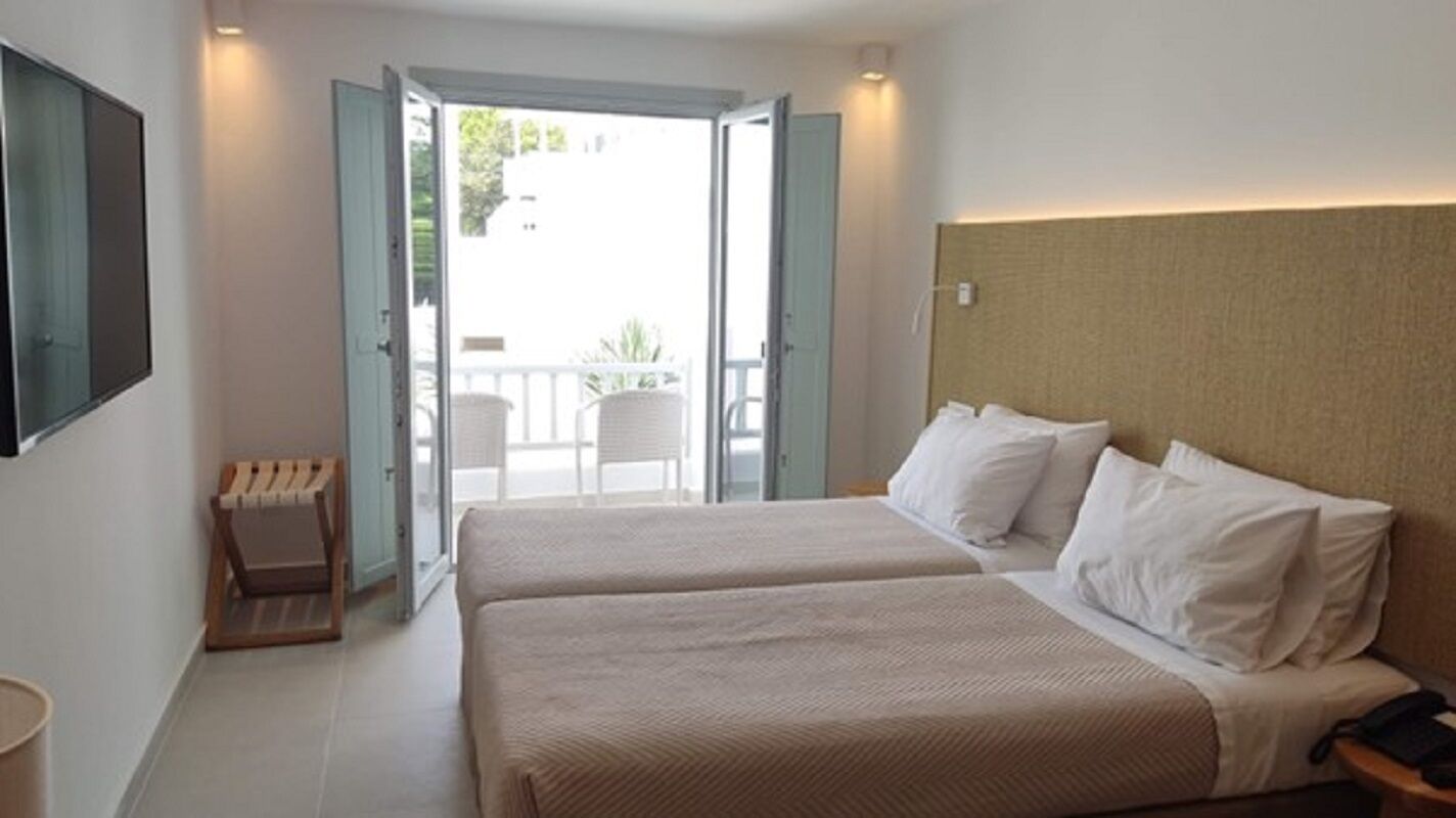Habitació d'hotel amb dos llits, una zona de seients petita i un balcó amb vistes.