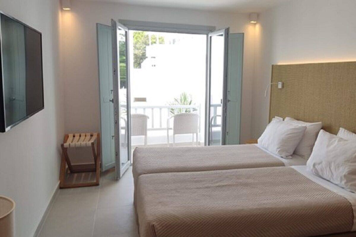 Habitación de hotel con dos camas, una zona de estar pequeña y un balcón con vistas.