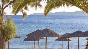 A beach with wooden lounge chairs and thatched umbrellas, overlooking a calm sea with distant mountains.