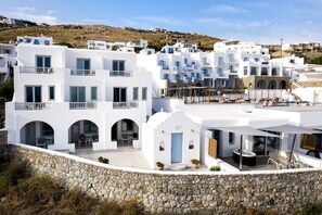 A coastal building with white walls, multiple balconies, and a stone retaining wall. - Manoulas Beach Mykonos Resort (Mykonos)