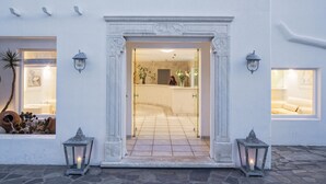 A hotel entrance with a white facade, a tiled floor, and two lanterns on either side.