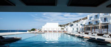 A modern hotel with a pool, white buildings, and a view of the sea.