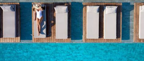 An aerial view of a poolside area with wooden loungers aligned along the edge, a clear blue pool, and a tiled deck.