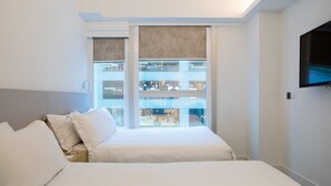 Quarto de hotel com uma cama, televisão fixada na parede e vista para um shopping.