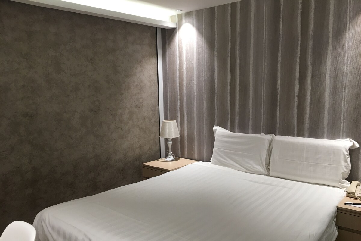 A hotel room with a large bed, a bedside table with a lamp, and a telephone.