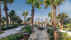 A pathway lined with palm trees and a wooden fence, leading to a covered area with a view of the beach.