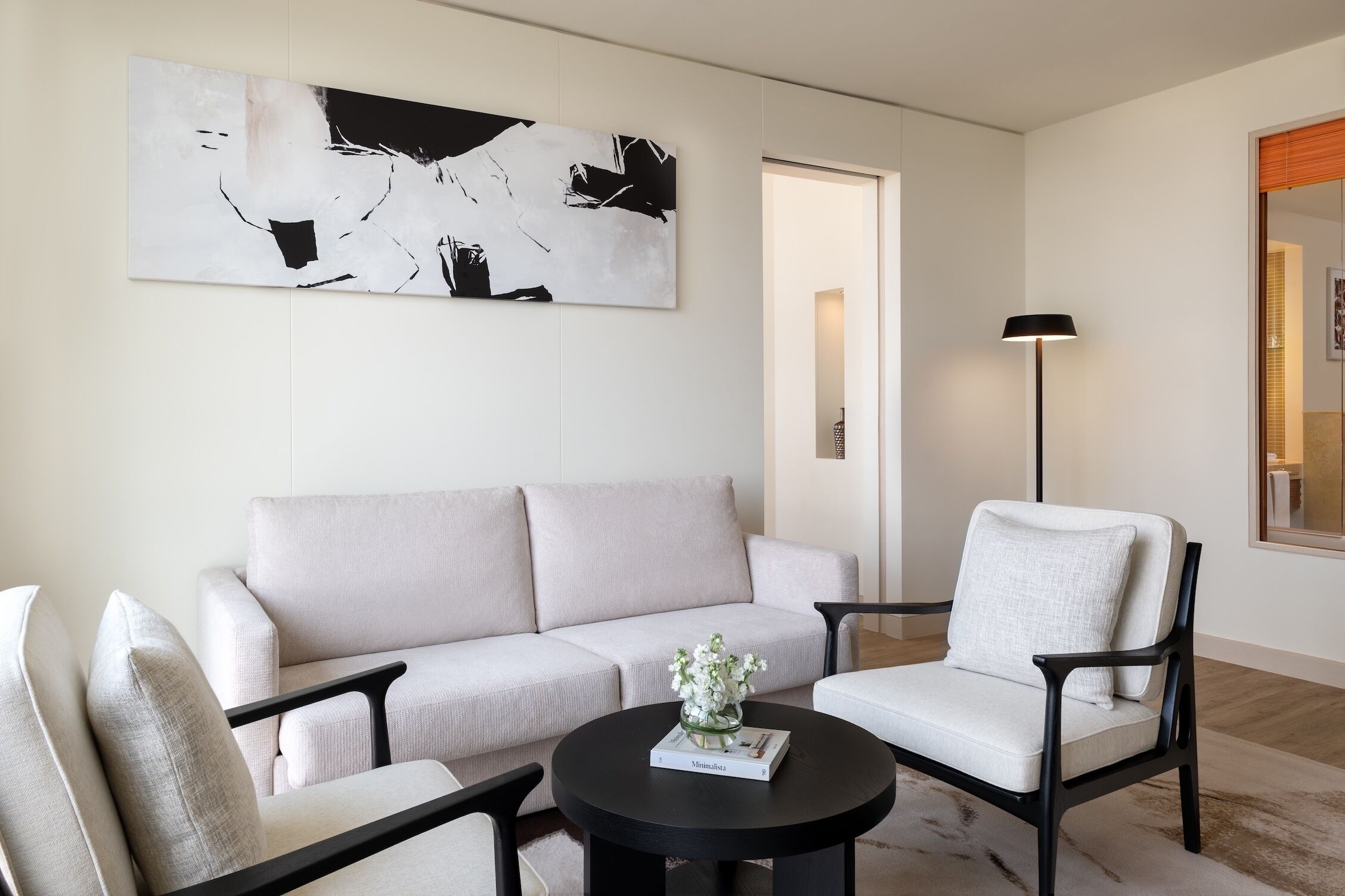 A modern living room with a sofa, two armchairs, a coffee table, and a large abstract painting on the wall.