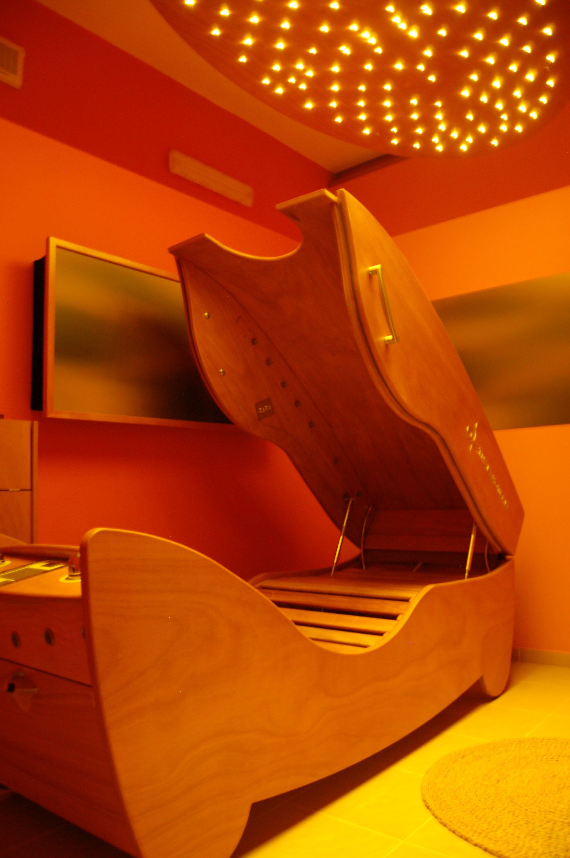 Una habitación con una cama de diseño único en madera, un televisor de pantalla plana montado en la pared y un techo con lámpara de techo con diseño.