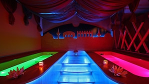 A spa area with two separate soaking tubs illuminated by blue and red lighting, a decorative wall with a mosque silhouette, and a small vase with a flower on each tub. - Hotel Residence Capo Campolato (Augusta)