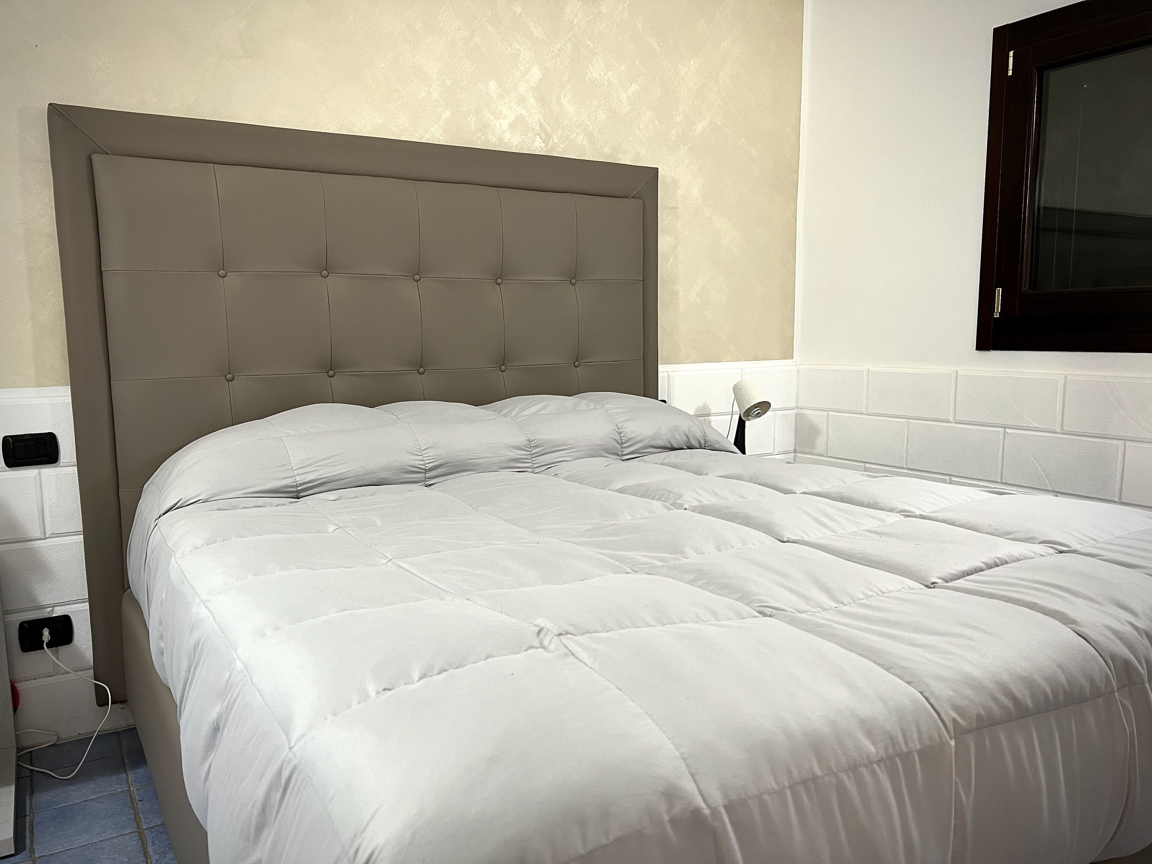 Un lit bien fait, avec une tête de lit capitonnée, du linge de lit blanc et une lampe de chevet.
