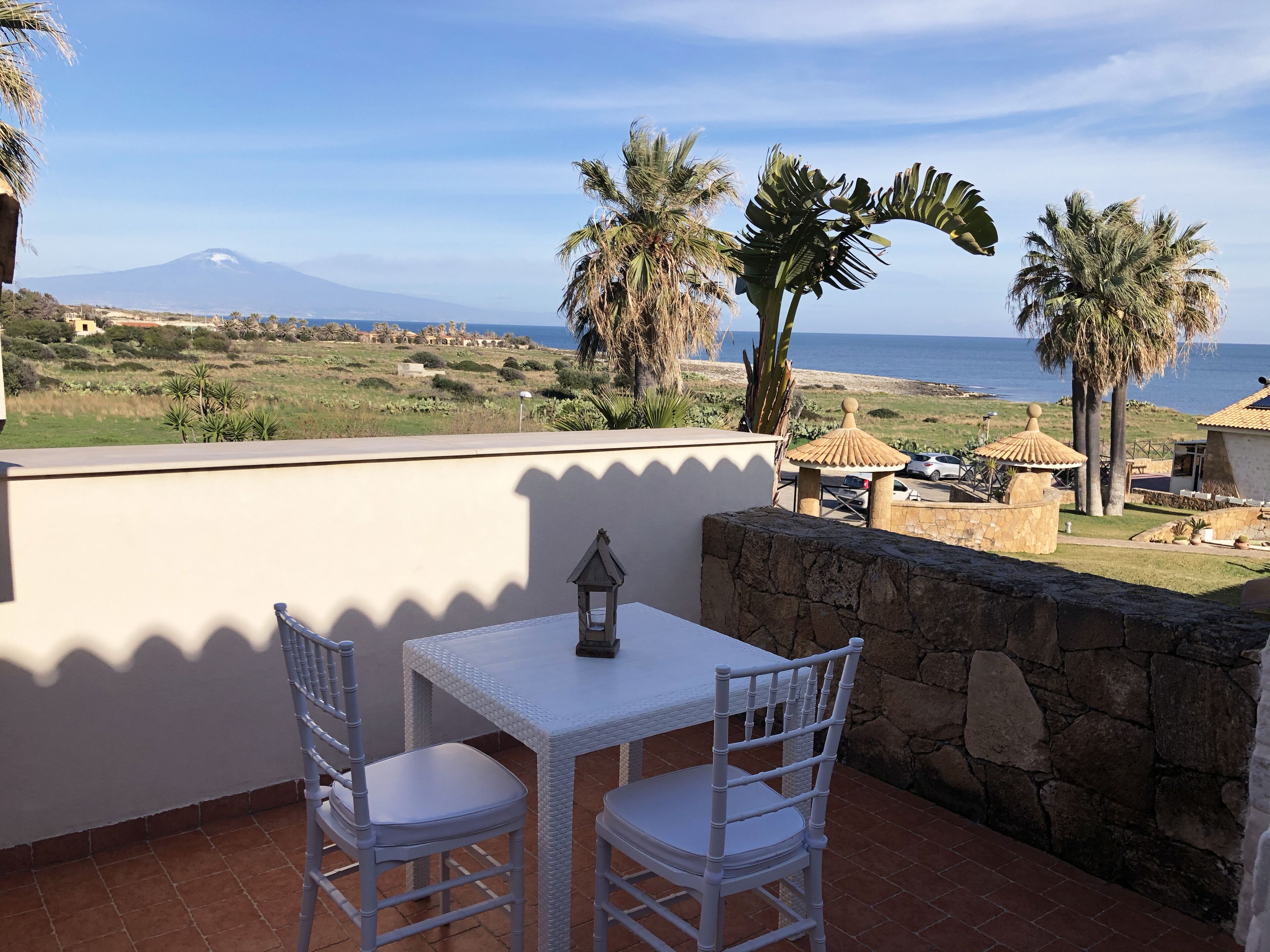 A balcony with a table and chairs, overlooking a beach and a mountain.