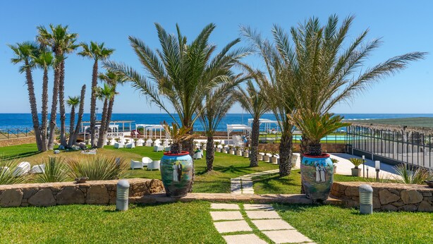 A landscaped outdoor area with palm trees, a pathway, and outdoor seating. - Hotel Residence Capo Campolato (Augusta)