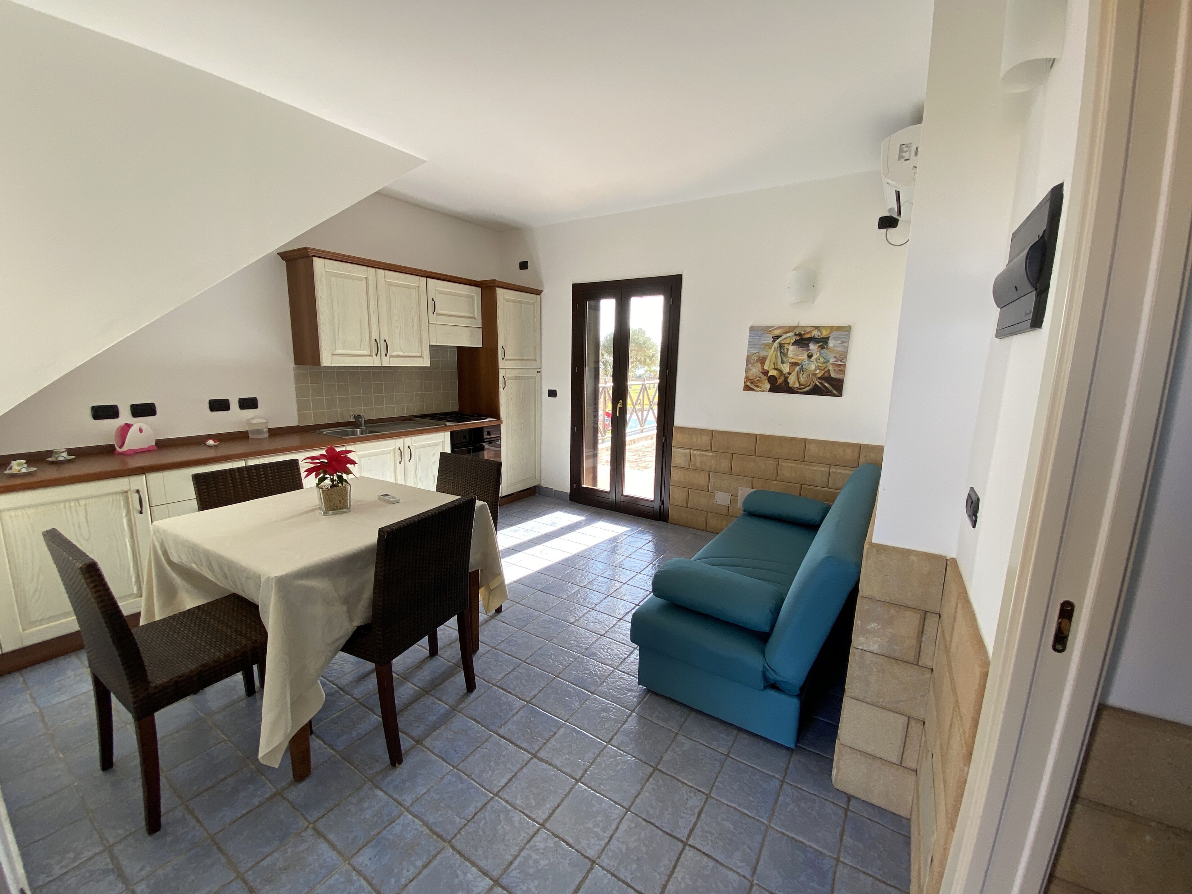 Una cocina compacta con armarios blancos, una mesa de comedor con sillas y un sofá azul.