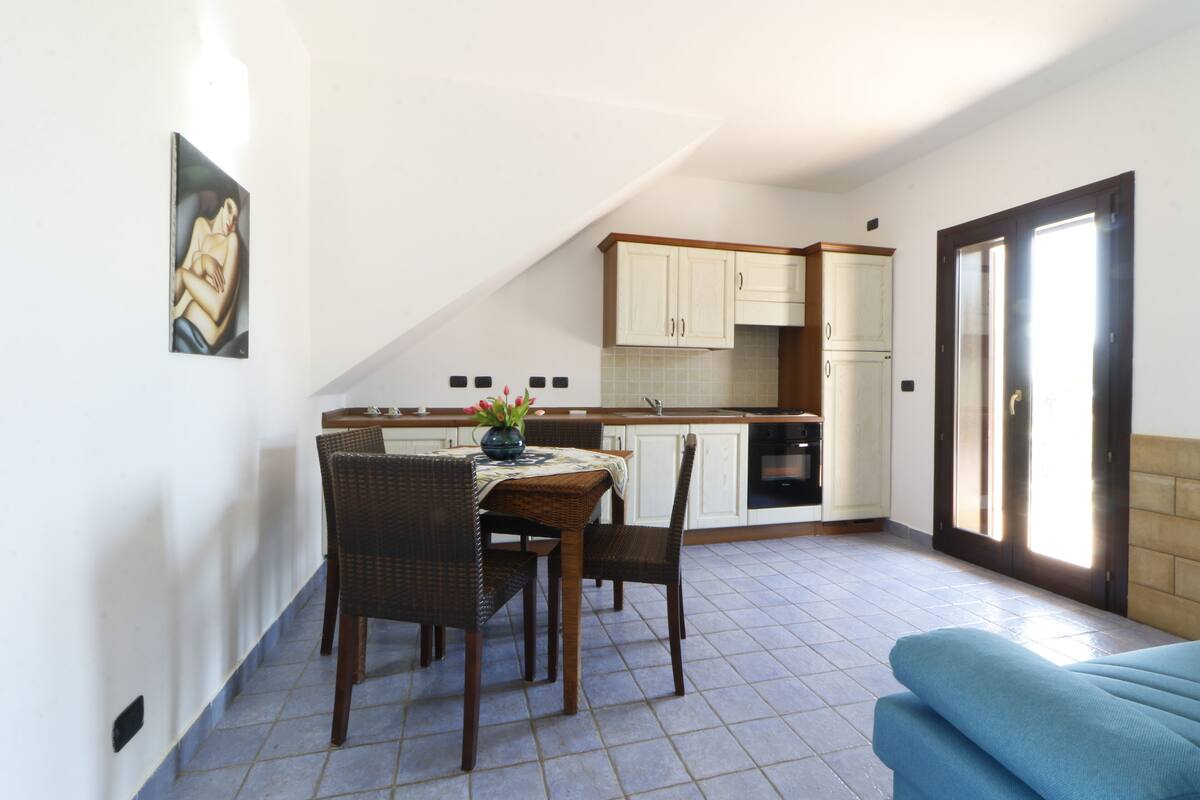 A compact kitchen with white cabinets, a dining area with wicker chairs, and a blue sofa.
