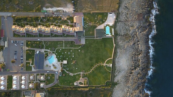 An aerial view of a coastal property with a swimming pool, parking area, and a rocky shoreline. - Hotel Residence Capo Campolato (Augusta)