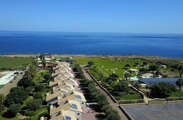 Un complejo turístico en la costa con edificios de varios pisos, una piscina y paneles solares.