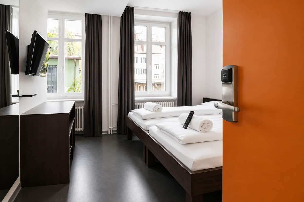 Una habitación de hotel con cama, escritorio, televisión y ventana con cortinas.