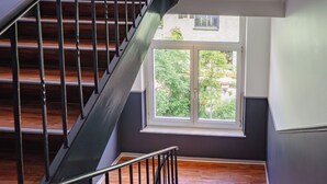 Una escalera de madera con barandillas metálicas, que lleva a una habitación con un ventanal que ofrece vistas al exterior, con vegetación.