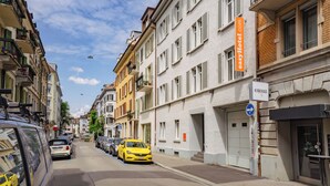 Vista de la calle con un coche amarillo estacionado al lado, edificios con balcones y un letrero que dice 'easyHotel.com'.