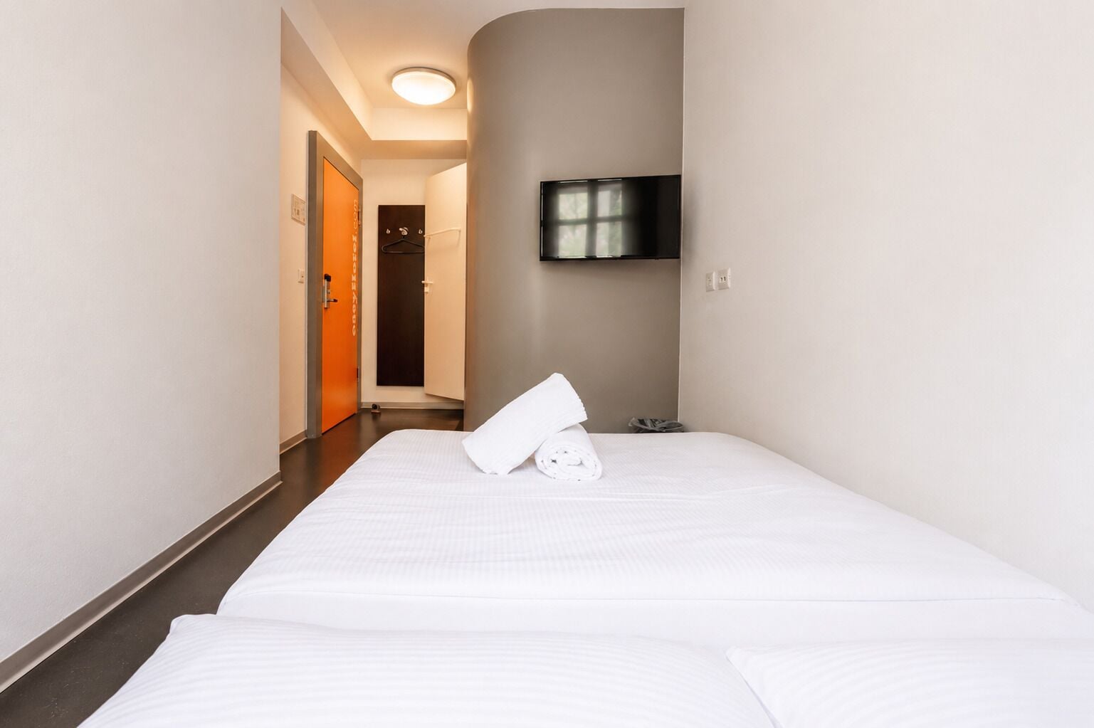 Une chambre d’hôtel avec un lit, un téléviseur fixé au mur et une porte donnant sur une salle de bain.
