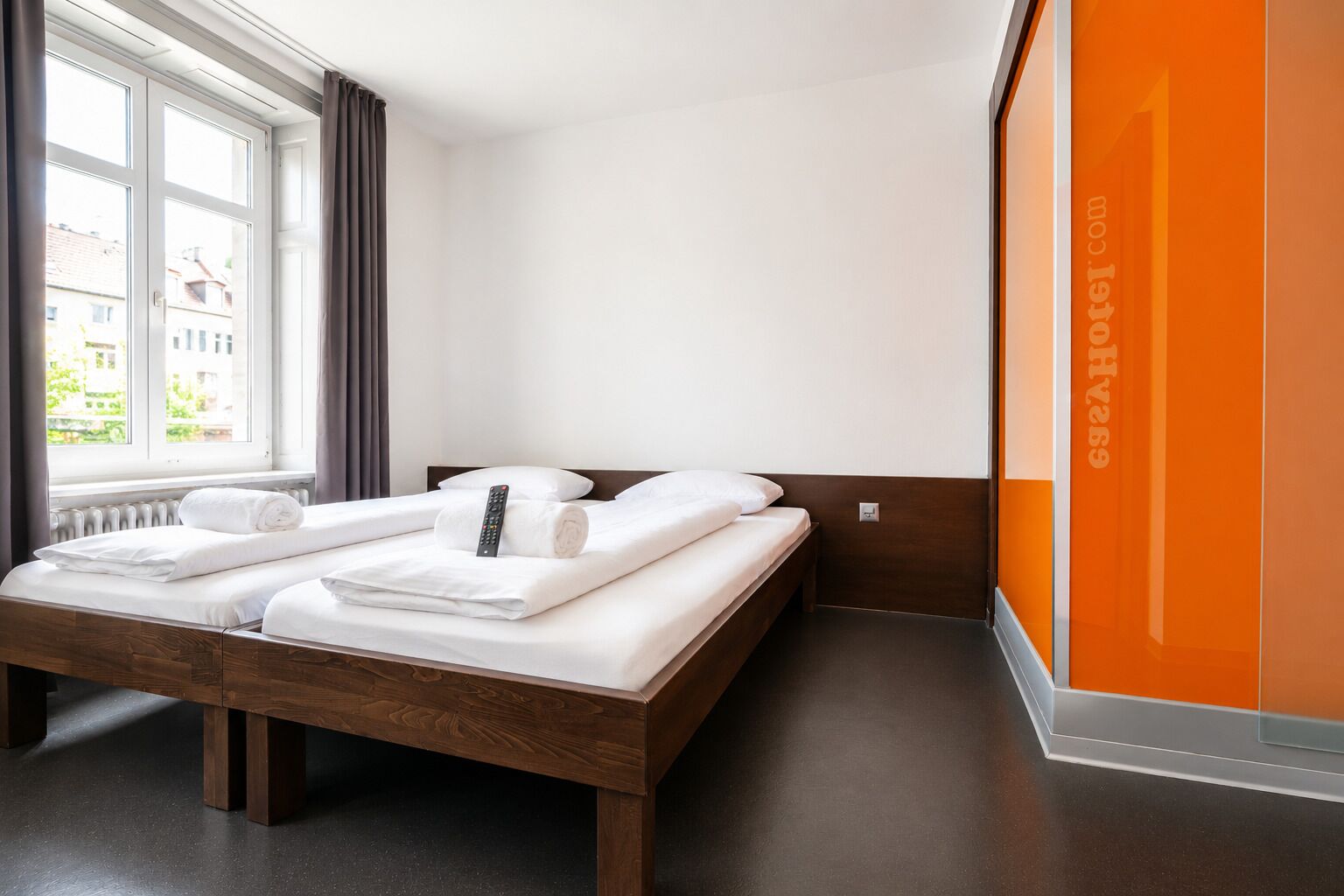 A hotel room with a bed, a window with curtains, a remote control, and a towel.