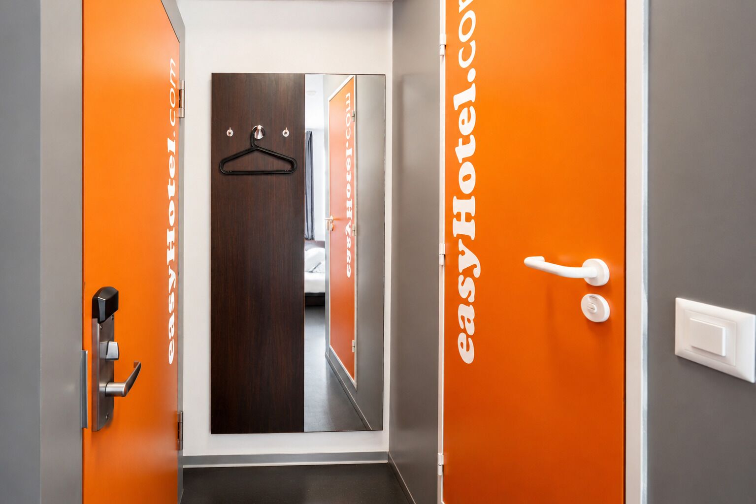 Un pasillo de hotel con una pared naranja, una puerta de madera y una puerta blanca con manija.
