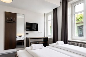 Une chambre d’hôtel avec un lit, une télévision, un miroir, une commode et une fenêtre avec des rideaux.