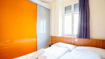 Une chambre d’hôtel avec un lit, une fenêtre avec des rideaux et un mur d’un orange vif.