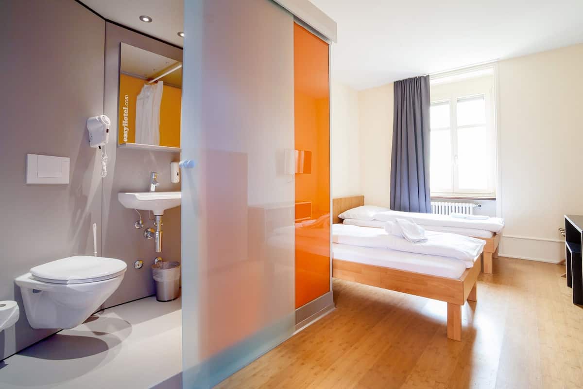 A modern hotel room with a bathroom, a bed, and a window.