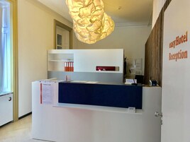 Una mesa de recepción con una placa identificativa, un tablón de anuncios y una lámpara colgante.