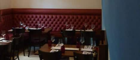 Un restaurante con un área de asientos en una cabina tapizada de rojo, mesas dispuestas para comer y una lámpara colgante.