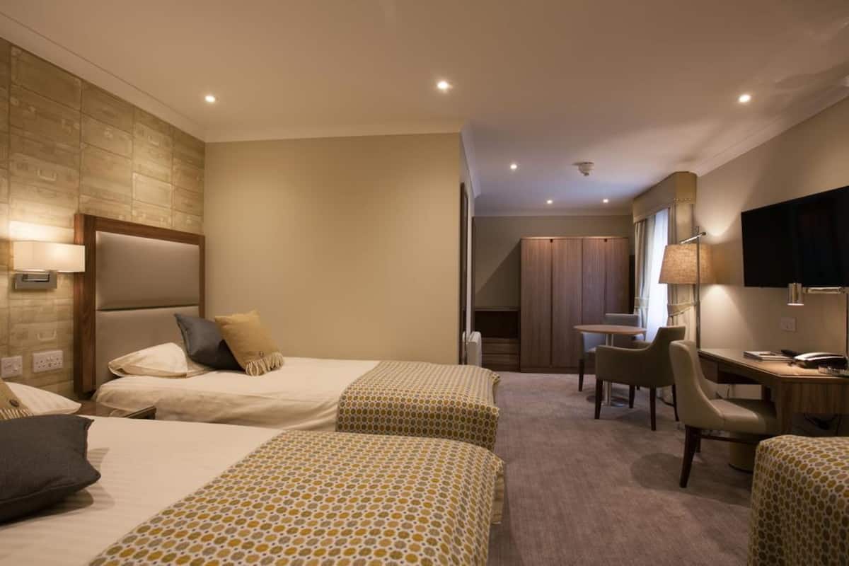 A hotel room with two beds, a desk, a chair, and a television.