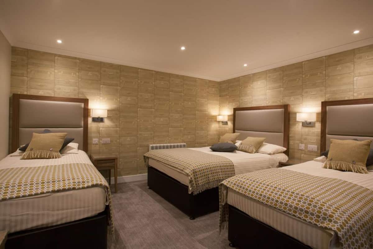 A hotel room with three beds, each with a headboard and bedside lamps.