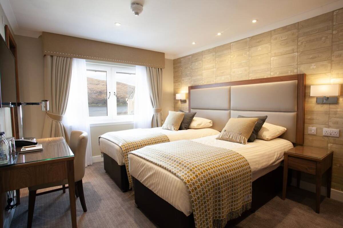 A hotel room with two beds, a desk, a chair, and a window with curtains.